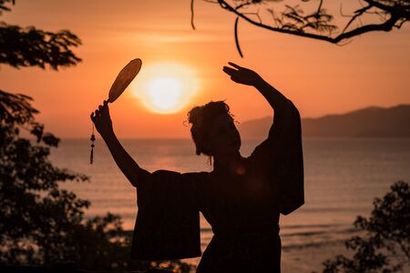 Silhouette of Japanese Geisha in kimono with fan at sunriseの写真素材