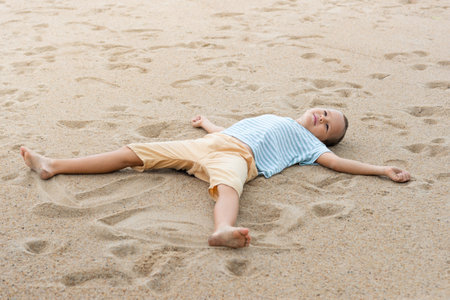 Outdoor portrait of a little cute boy laying on the sandy beach.
