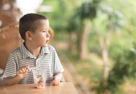 Cute boy eating ice-cream in outdoor cafeの写真素材