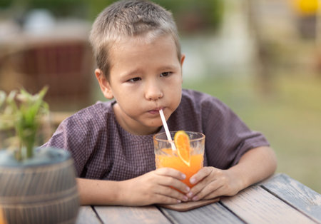 Cute boy drinking juice in outdoor cafeの写真素材