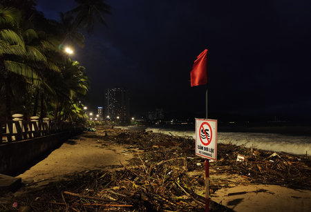 Nha Trang beach during the intense rainy season after a powerful storm: high waves, scattered tree branches, bushes, and marine debris washed ashore.の写真素材