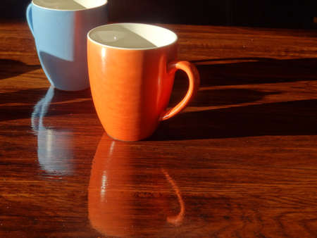 Close up of breakfast cups and shadows on wood grain table.の写真素材