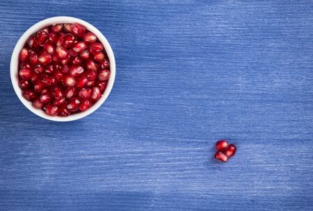 pomegranate seeds in a pipkin on a wooden surfaceの写真素材