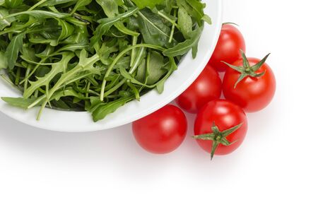 fresh rucola leaves in a bowl and tomatoes, isolated on whiteの写真素材