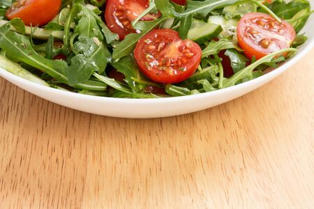 salad from ruccola, cherry tomatoes and cucumber, on wood tableの写真素材