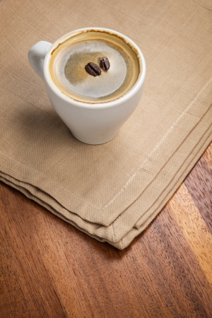dark espresso in a cup and two beans on burlap surfaceの写真素材