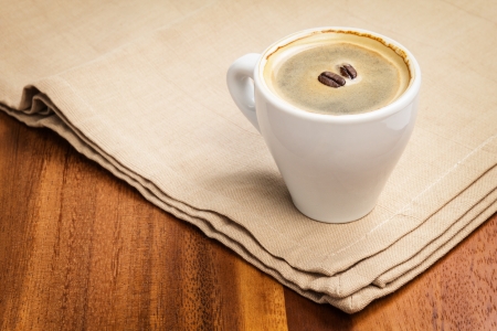 dark espresso in a cup and two beans on burlap surfaceの写真素材