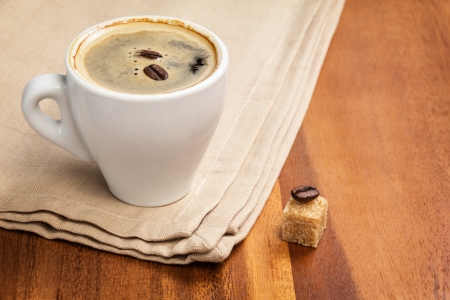 dark espresso in a cup and two beans on burlap surfaceの写真素材