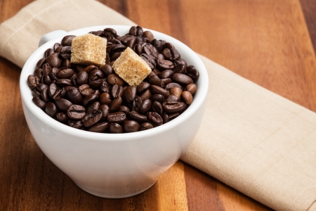 heap of coffee beans in cup with cane-sugar, on brown wood tableの写真素材