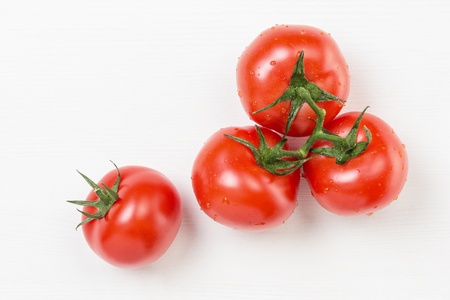 red tomatoes with branch, on white wood tableの写真素材