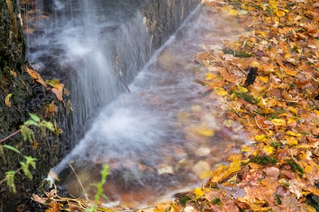 small waterfall in autumn park, with heap of leavesの写真素材