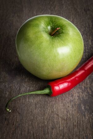 ripe green apple and chili pepper close up, on old wood tableの写真素材