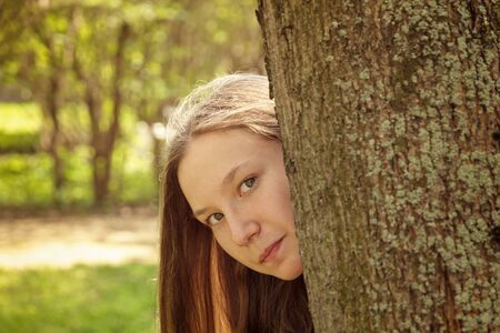 portrait of young teenager girl hiding behind tree, summer timeの写真素材