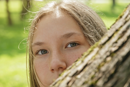 portrait of young teenager girl hiding behind tree, summer timeの写真素材