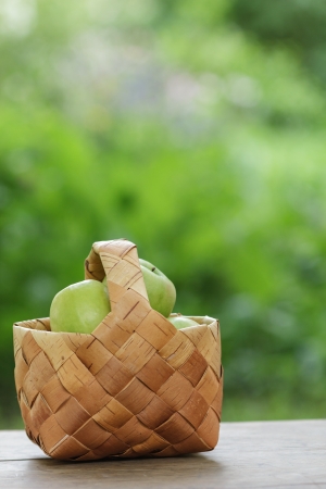green apples in a birchbark basket, on wooden tableの写真素材