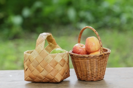 green and red apples in a basket, on wooden tableの写真素材