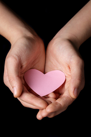 female teen hands holding heart paper, isolated on blackの写真素材