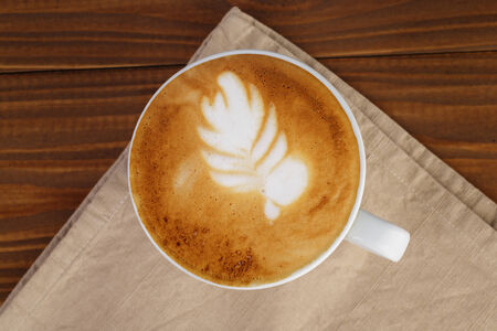 freshly made cup of cappuccino with leaf art, on wooden tableの写真素材