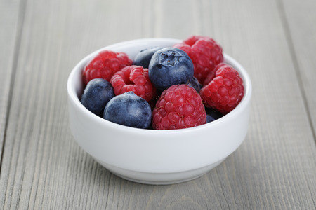 raspberries and blueberries in white bowl, on old wood table
