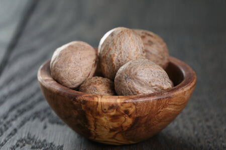 whole nutmegs in olive bowl on oak table, rustic style