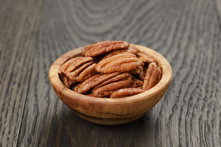 pecan nuts in olive wood bowl on oak table, rustic style