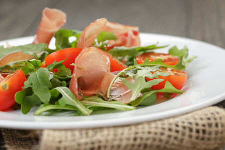salad with prosciutto arugula and tomatoes on wooden tableの写真素材