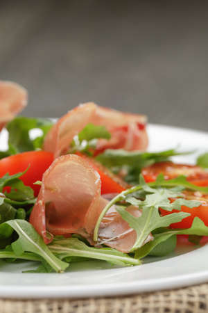salad with prosciutto arugula and tomatoes on wooden tableの写真素材