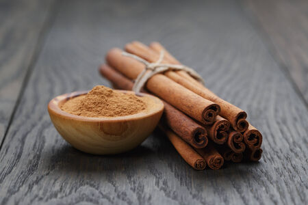 bunch of cinnamon sticks tied with twine and powder in bowl, on rustic oak tableの写真素材