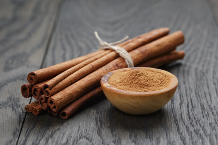 bunch of cinnamon sticks tied with twine and powder in bowl, on rustic oak tableの写真素材
