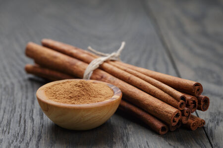 bunch of cinnamon sticks tied with twine and powder in bowl, on rustic oak tableの写真素材
