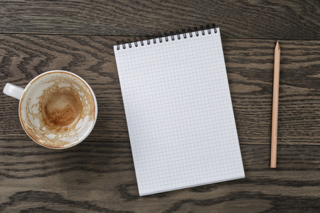 Blank notepad with pencil and empty coffee cup on wooden table, office themeの写真素材