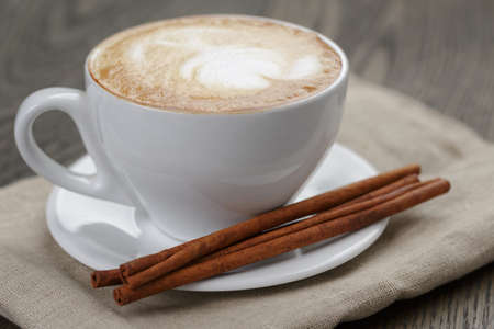 cup of cappuccino with cinnamon sticks, on old tableの写真素材