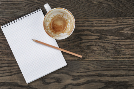 Blank notepad with pencil and empty coffee cup on wooden table, office themeの写真素材