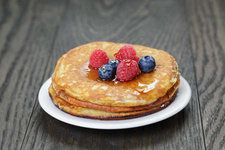 Pancakes with raspberry, blueberry and maple syrup, on oak wooden tableの写真素材