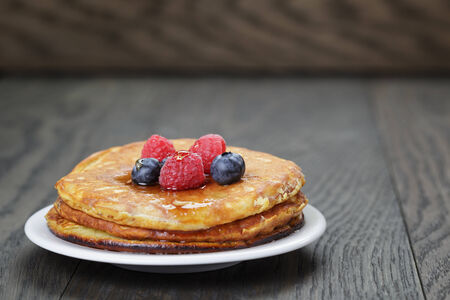 Pancakes with raspberry, blueberry and maple syrup, on oak wooden tableの写真素材