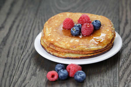 Pancakes with raspberry, blueberry and maple syrup, on oak wooden tableの写真素材