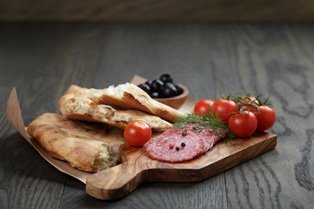 Antipasti with salami, olives, tomatoes and bread on wod tableの写真素材