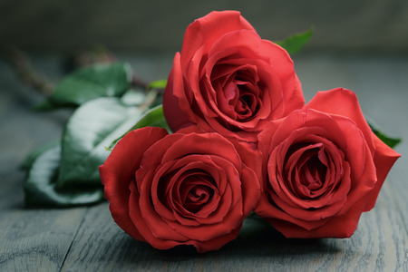 three red roses on old oak tableの写真素材