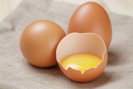 whole and broken raw brown eggs closeup on wood tableの写真素材