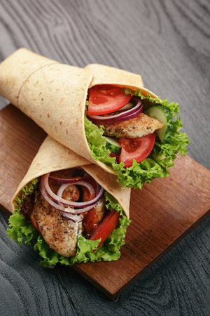 pair of fresh juicy tortilla wraps with chicken and vegetables, on tableの写真素材
