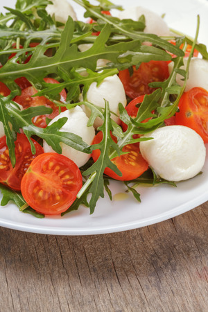 salad with mozzarella cherry tomatoes and arugula, close up on wood tableの写真素材