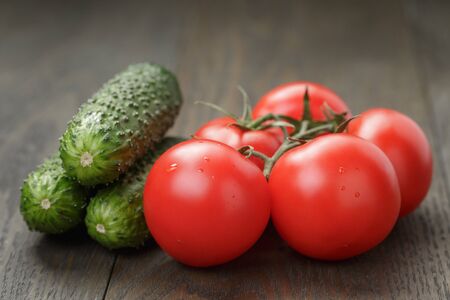 ripe wet tomatoes on vine and cucumbers on wood tableの写真素材