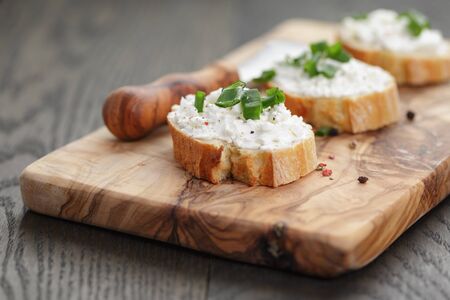 crunchy baguette slices with cream cheese and green onion on olive boardの写真素材