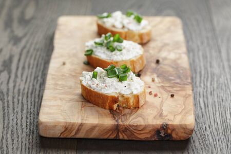 crunchy baguette slices with cream cheese and green onion on olive boardの写真素材