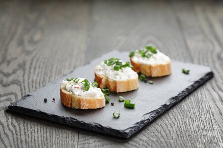 crunchy baguette slices with cream cheese and green onion on slate board