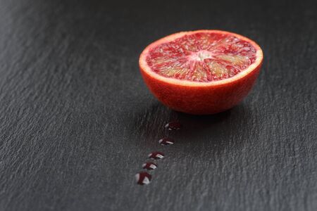 red sicilian orange sliced on slate board with juice dropsの写真素材