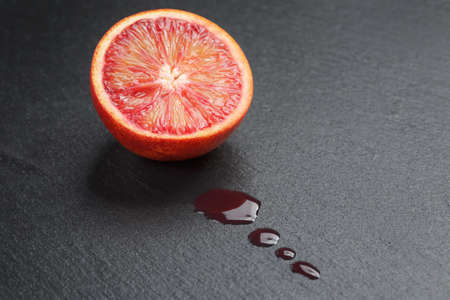 red sicilian orange sliced on slate board with juice dropsの写真素材