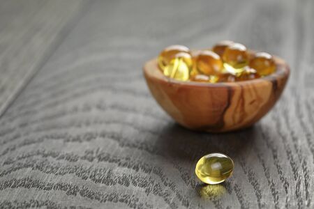 fish oil capsules in wood bowl on wooden tableの写真素材