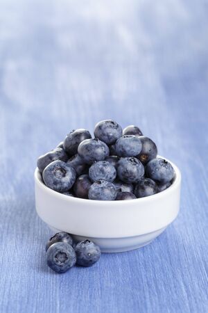 heap of fresh washed blueberries in white bowl on blue wood tableの写真素材
