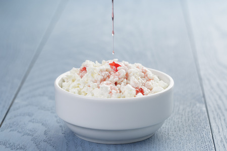 cottage cheese with strawberry jam in white bowl on blue wooden tableの写真素材